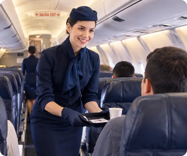 Comissária de bordo com uniforme azul, sorrindo enquanto serve um café a um passageiro na cabine do avião